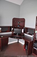 Full view of corner computer desk with cherry finish, showing the central hutch with small lamp and two side hutches, keyboard tray with keyboard and mouse, computer monitor on desk surface.