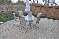 Full set overview on stone patio showing table, six chairs, and umbrella closed