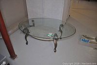 Oval glass coffee table showing the full metal base and clear glass top on a solid floor surface.