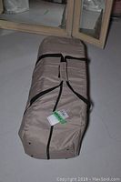 Beige soft-sided carrying bag containing a Pack and Go playpen, secured with black straps and showing an Eddie Bauer logo embroidered on the side.