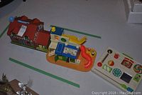 Three vintage Fisher Price toys shown on a white surface, including a house, Sesame Street Clubhouse, and activity tray.