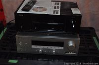 Two AV receivers stacked, Denon on top with manuals and remote, Yamaha below
