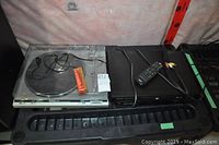 Turntable and DVD player side by side on plastic surface with wires and remote control visible.