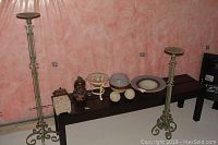 Photo of two metal candle stands, various decorative boxes, potpourri dishes, and two decorative balls arranged on a bench against a pink mottled wall.