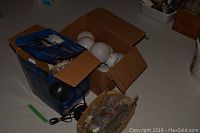 Photo showing boxes containing eight white globe builder's lights and a small black desk lamp with cables visible.