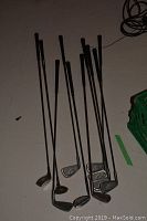 Ten left-handed golf irons and two putters arranged on floor, showing full lengths of clubs and grips.