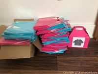 Stack of pink and blue flat packed product boxes in cardboard storage box and on floor, some pink boxes have business stickers