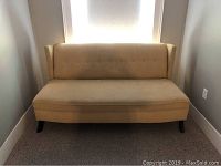 Photo of a yellow vintage wing sofa against a wall beneath a window, showing full view of the sofa upholstery and legs.