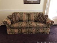 Front view of patterned upholstered sofa with three back cushions and bolster arm pillows.