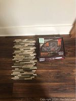 One box of Neo Splash brand glass backsplash tiles in earth tones next to a single tile sheet showing multi-material rectangular pattern of glass and stone pieces.