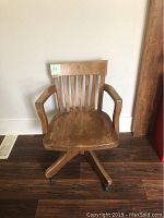 Front view of the vintage wooden office chair showing slatted backrest, armrests, and worn wooden seat.