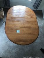 Top view of the dining table in its elongated oval form with a medium brown maple finish and sectional top boards.