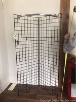 Photo of one black metal grid panel set up in a corner with a silver hanging bar on top, showing size and condition
