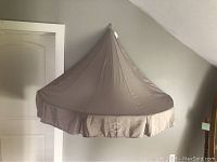 Beige fabric child's room wall hanging tent canopy hanging from wall, pointy tent shape with pleated skirt edge.