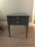Front view of the vintage side table showing two drawers with metal pulls, painted dark gray with carved leg details.