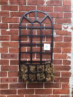 Black metal wall planter fixed on brick wall showing arched trellis design and coir lined basket base.