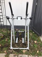 Silver and black elliptical exercise machine shown outdoor on grass. Missing rubber heel stops as noted.