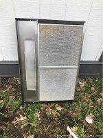 Front face of the black overhead range hood vent showing two rectangular metal mesh filters for grease and a built-in rectangular light panel on one side.