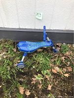 Blue toddler bike with training wheels viewed from the side on grass and leaves