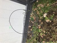 Circular metal basket frame lying on grass, showing its shape and structure.