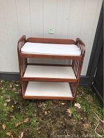 Front view of wooden baby change table outdoors showing cushioned changing pad and two lower shelves