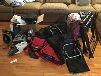 Overview showing luggage stands, rolling bag, suitcases, vacuum, fan, and duffel bags arranged on floor in front of couch.