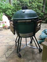 Full view of the Big Green Egg grill on metal stand with wooden shelves and caster wheels