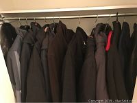 13 men's outdoor coats hanging on a closet rod, mainly dark colors including black, brown and gray, showcasing overall collection.