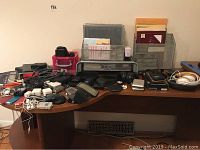 Photo shows multiple electronic devices, chargers, and accessories on a desk surface, including various cables and storage organizers.