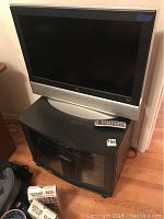 Vizio flat screen TV on black TV stand with remote on top, wooden floor background.