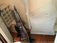 Photo showing vacuum cleaners: Hoover Linx cordless and Shark upright next to plastic storage containers and shelving unit.