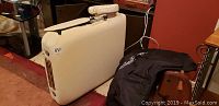 Folded white massage table showing overall condition and black carry bag beside it.