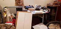 Overall view of art supplies piled on and around a table, showing canvases, bags, and art books.