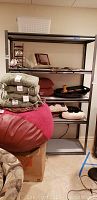 Full view of metal shelving unit with various items on shelves including fabric items, cushions, and decorative objects to show shelving condition and stain presence.