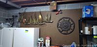 Wide shot showing metal wall-mounted candelabra on left, seven metal sailboats in center, and large metal sun wall decor on right, all mounted on pegboard wall.