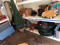 Wide angle view of storage shelves showing a 71 inch tall lighted faux bush in brown planter, green wreath storage bags, small bowls, and other household items.