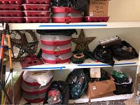 Shelving unit with wreath storage boxes, cast iron tree stands, wreath, ornaments, wall star decorations, and boxes with Christmas lights and decor