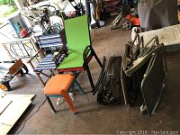 Wide view of the lot showing two orange plastic side tables, several chairs including green camp chair and two folding chaises stacked, and two folded chairs.