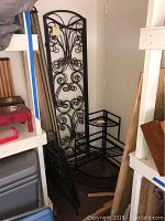 Two black metal framed wall dividers with three panels each leaning against a wall beside two black metal folding corner plant stands.