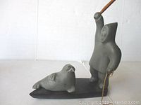 Stone carving of Inuit hunter wielding spear standing on base with seal figure in front