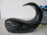 Side view of black stone whale carving next to soda can for scale, showing curved tail and body details.