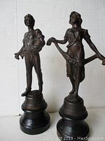 Frontal view of the bronze man and woman figurines on black wooden bases, showing size and posture.