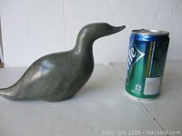 Profile view of the stone bird carving next to a soda can for size reference, showing the rounded body and curved beak.