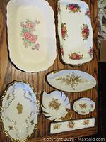 Top view of seven vintage fine bone china trays and dishes, showcasing floral and gold rim details on wooden surface.