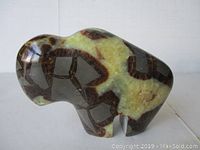 Side view of polished bison stone carving showing natural brown and cream patterns and rounded shape.