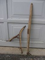 View of two rustic old farm horse haynes pieces leaning against a garage door on concrete, showing full shape and condition.