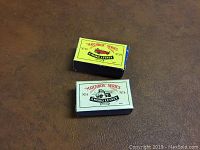 Two original Matchbox Series boxes, one yellow-green labeled No.19 and one white labeled No.76, placed on brown surface