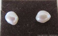 Close-up of the two freshwater pearl studs showing their irregular shape and luster on dark background.