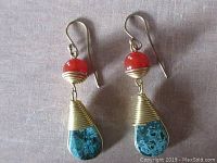 Close-up of pair of drop earrings showing orange carnelian round beads on top and blue-green turquoise teardrop stones wrapped in brass wire below them with brass earwires.
