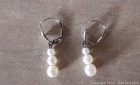 Pair of vintage cultured pearl drop earrings with three round pearls on each earring lying flat showing front side
